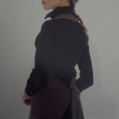 Pessoa em perfil com camisola preta, avental castanho e boina castanha