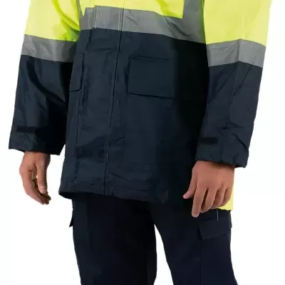 Homem com vestuário de segurança amarelo e azul com faixas refletoras e calçado cinzento