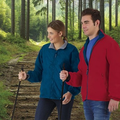 Duas pessoas vestem blusões de tecido polar azul e vermelho numa floresta, segurando bastões de caminhada