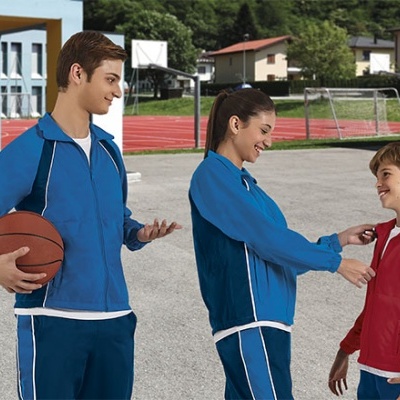 Três jovens em fatos de treino azul e vermelho num campo desportivo com pista de atletismo ao fundo