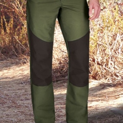 Calças de homem verdes e pretas com reforços nos joelhos, ambiente exterior com chão de terra