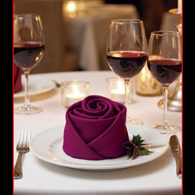 Mesa de restaurante com guardanapo roxo em forma de rosa e copos de vinho