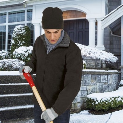 Homem com roupa de inverno a usar uma pá para neve em frente a casa com neve.