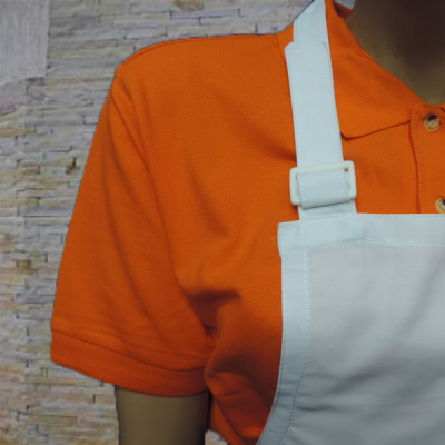 Manequim com camisa polo laranja e avental branco contra parede de pedras clara