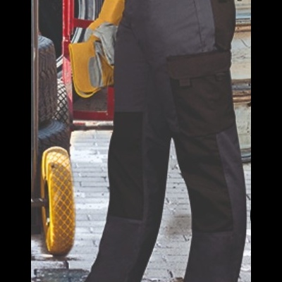 Calças de trabalho bicolores pretas e cinzentas com bolsos, pessoa segura luvas amarelas e cinzentas em ambiente de trabalho com pneus e carrinho.