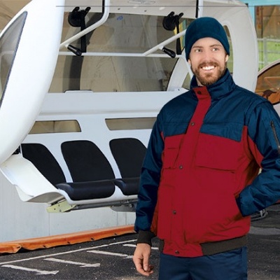 Homem com casaco azul e vermelho ao lado de teleférico branco