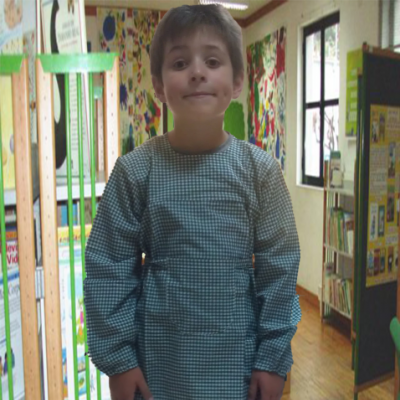 Criança com bata escolar verde em ambiente escolar interior.