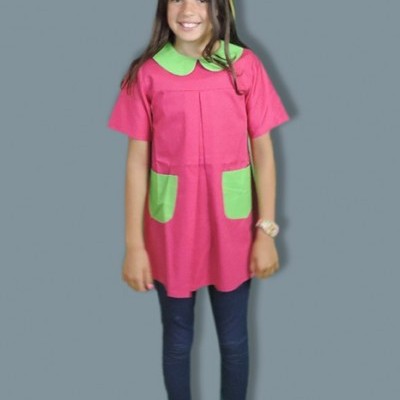 Menina com túnica rosa e verde, calças azuis escuras e meias vermelhas em fundo cinza