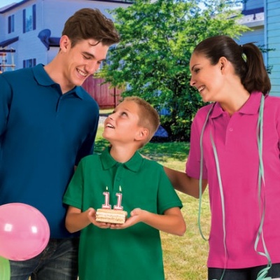 Três pessoas com camisolas tipo polo coloridas e bolo de aniversário no exterior