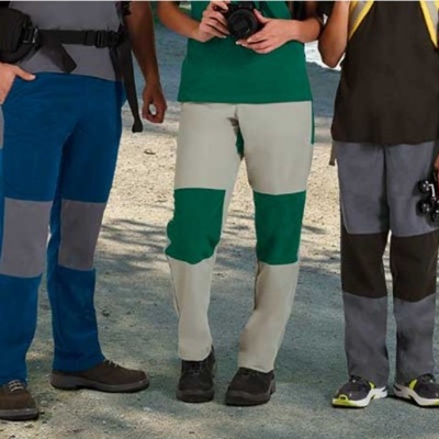 Três pares de calças reforçadas em várias cores num ambiente ao ar livre.