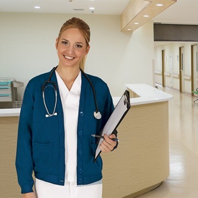 Enfermeira sorridente com jaleco azul e estetoscópio em corredor de hospital