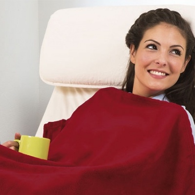 Mulher sorridente sentada numa cadeira branca com uma manta vermelha e uma caneca amarela