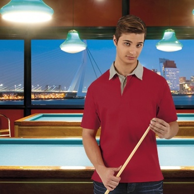 Homem jovem com polo vermelha e gola cinzenta segurando taco de bilhar em sala com mesa de bilhar e vista noturna da cidade