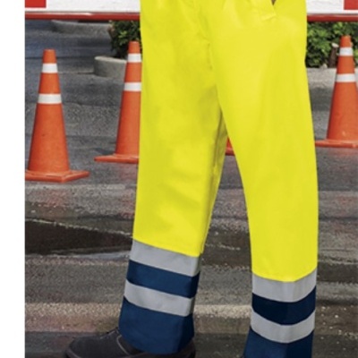 Calças de trabalho amarelas com faixas refletoras e calçado preto em ambiente urbano