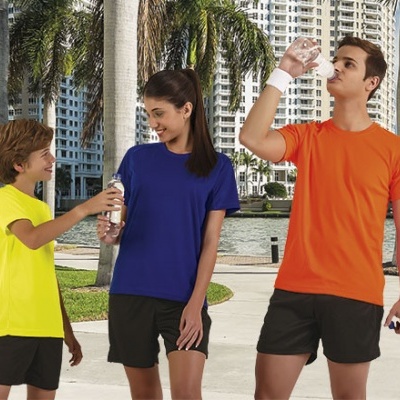 Três jovens ao ar livre com t-shirts coloridas e calções pretos junto a palmeiras e edifícios.