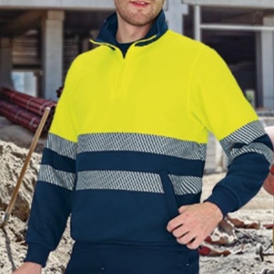 Camisola de alta visibilidade amarela e azul escuro com faixas refletoras e calças azuis num canteiro de obras