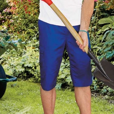 Pessoa com calções azuis segurando pá num jardim com relva e plantas