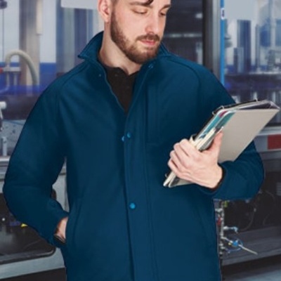 Homem com casaco azul escuro e camisa preta segurando cadernos em ambiente industrial