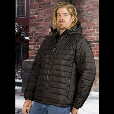 Homem com casaco acolchoado preto de capuz, fecho de correr e punhos elásticos, em cenário urbano com neve e parede de tijolos.