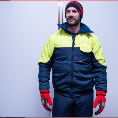 Homem com uniforme de proteção amarelo e azul escuro, luvas vermelhas e gorro preto com vermelho