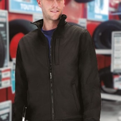 Homem com casaco preto e calças azuis num ambiente de oficina com pneus ao fundo