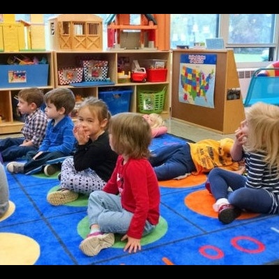 Crianças sentadas num tapete colorido numa sala de aula com mobiliário e brinquedos