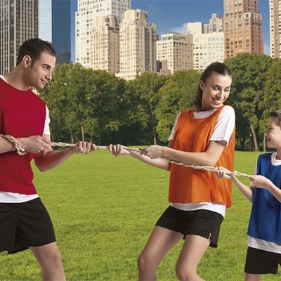 Homem, mulher e criança a jogar cabo de guerra em campo verde com coletes coloridos