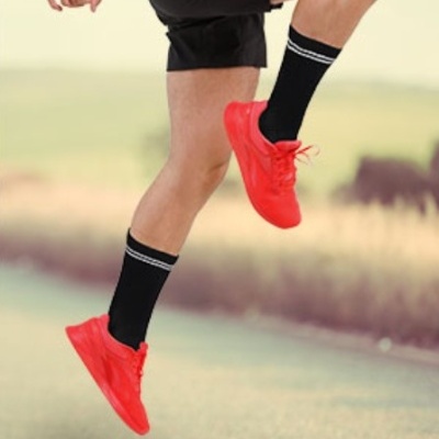 Pessoa a saltar usando ténis vermelhos, meias pretas e calções pretos numa estrada ao ar livre