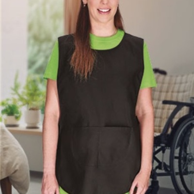 Pessoa com bata preta sobre roupa verde em ambiente interior com cadeira de rodas