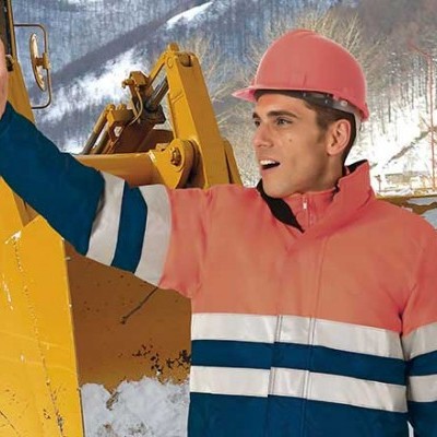 Homem com casaco de proteção laranja e capacete rosa junto a máquina amarela na neve