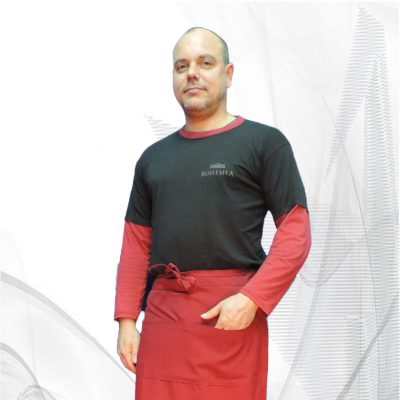 Homem com t-shirt preta e vermelha, avental vermelho e calças jeans em fundo branco com linhas cinzentas