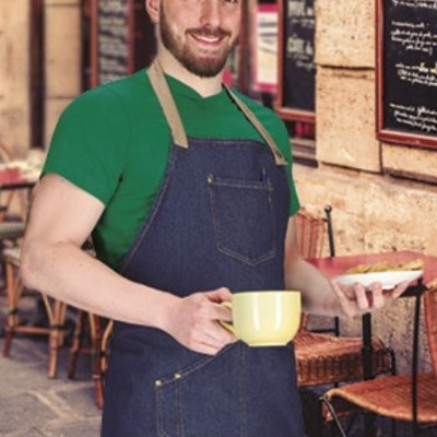 Homem com avental de ganga e camiseta verde segurando chávena amarela numa esplanada
