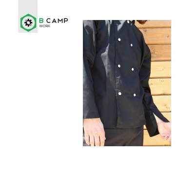 Uniforme de trabalho preto com botões brancos e logotipo B CAMP WORK junto a parede de madeira