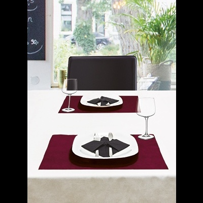 Mesa posta com pratos, guardanapos pretos, jogos americanos bordô, taças e cadeira preta junto a uma janela com plantas