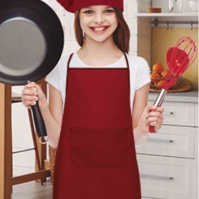 Menina com chapéu e avental vermelho segurando frigideira preta e batedor vermelho numa cozinha clara