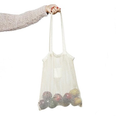 Saco de rede branco com alças finas cheio de frutas coloridas, segurado por mão com camisola cinzenta