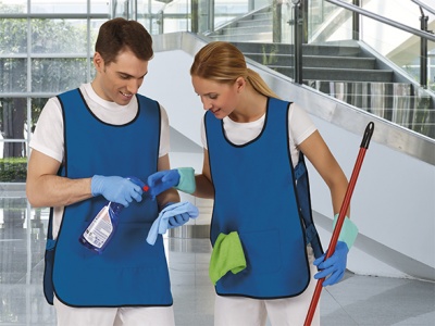 Duas pessoas com coletes azuis, luvas e produtos de limpeza em edifício interior com escadas.