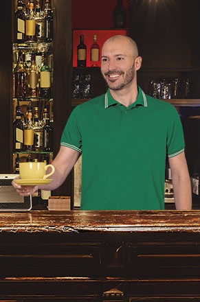 Homem de polo verde segurando chávena amarela num bar
