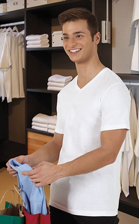Homem jovem com camisa branca segurando roupa azul claro numa loja de roupa