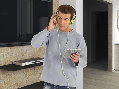 Homem a ouvir música com auscultadores amarelos e leitor de cassetes prateado, em ambiente interior com parede de pedra