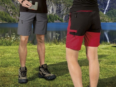 Dois homens com calções curtos e botas de caminhada numa paisagem com lago e montanhas