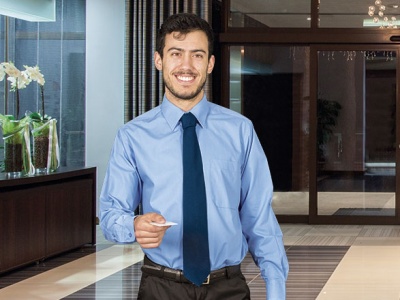 Homem com camisa azul clara e gravata azul escura junto a um cartão branco em ambiente interior elegante