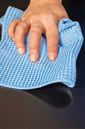 Mão a limpar superfície preta com pano azul texturizado