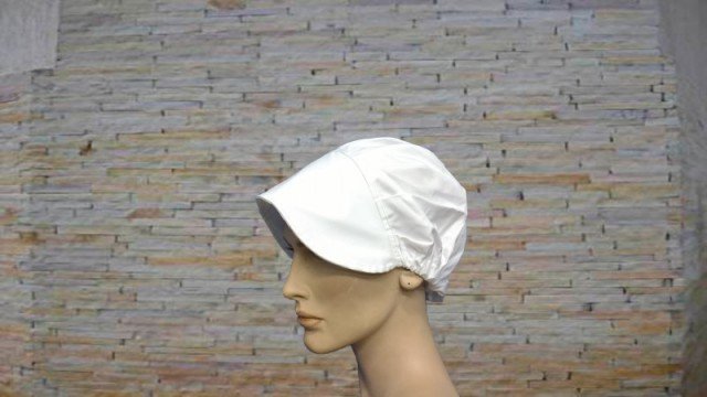Chapéu branco de tecido em manequim com parede de tijolos ao fundo