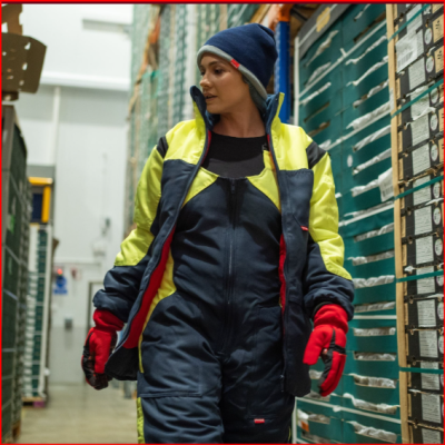 Pessoa em macacão de trabalho azul e amarelo, luvas vermelhas e gorro azul num armazém