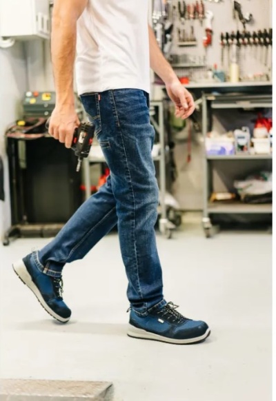 Pessoa calçando sapatos desportivos azuis e calças de ganga num ambiente de oficina