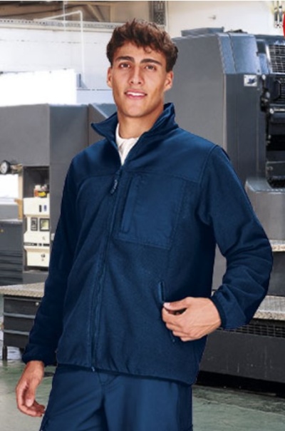 Homem com casaco azul escuro com fecho, em ambiente industrial