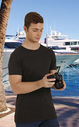 Homem com t-shirt preta segurando câmara fotográfica ao ar livre junto ao mar.