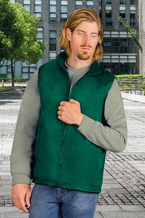 Homem com colete verde escuro felpudo, manga cinza clara e jeans azul em ambiente urbano