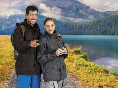 Casal com casacos impermeáveis pretos junto a lago e montanhas